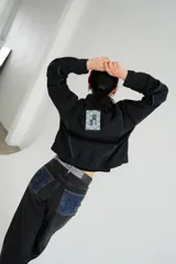 Campera de jean negra, tipo bomber, con cuello, puños y cintura elásticos. Presenta un parche cuadrado en la espalda con un diseño geométrico y la palabra "KSLEY".