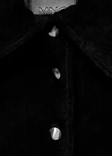 Chaqueta corta de piel bovina serraje color negro, con cuello camisero, bolsillos de parche con solapa en el frente, manga larga y cierre frontal de botones.