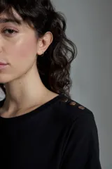 Remera negra de manga corta con detalle de botones metálicos en el hombro. Corte recto y cuello redondo.