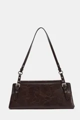Bolso de hombro de formato alargado, color marrón oscuro con acabado ligeramente desgastado. El asa de hombro es delgada y ajustable mediante hebillas metálicas. Presenta detalles de tachas o remaches metálicos en los puntos de unión del asa.