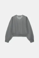 Chaqueta estilo bomber de punto color beige con acabado brillante, cuello redondo, manga larga con puños elásticos y cierre frontal con cremallera.