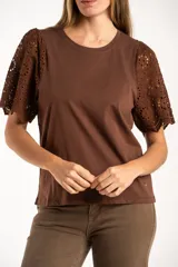 Remera de algodón peinado color negro, con mangas cortas de broderie con diseño calado y terminación festoneada. Presenta un corte oversize y cuello redondo.