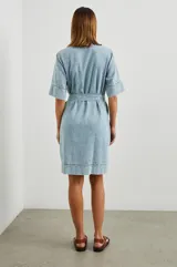 Vestido camisero corto de denim celeste con cuello en V, mangas cortas y cinturón de lazo. Presenta bolsillos laterales y pespuntes a contratono.