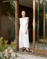 Vestido largo de lino blanco con calce holgado, bolsillos delanteros, volados en los hombros y detalle de pespunte en color beige.
