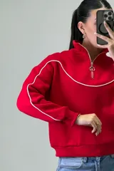 Buzo deportivo color beige con cuello alto y cierre frontal parcial. Presenta costuras decorativas con ribetes blancos en el pecho y a lo largo de las mangas. Posee puños y ruedo elásticos.