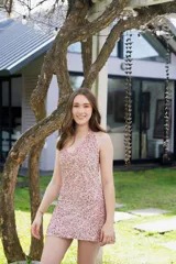 Vestido corto color fucsia con escote en V, breteles finos que se atan al cuello, corte a la altura de la cadera y falda acampanada con ruedo irregular.