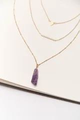 Collar dorado de múltiples capas con cadena de eslabones y cuentas, cadena con dije de triángulo, cadena con dije de barra horizontal y cadena con dije de amatista.