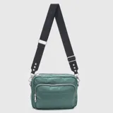 Cartera tipo bandolera de la marca Bubba, confeccionada en material sintético de acabado satinado en color verde. Presenta un diseño rectangular con tres compartimentos exteriores con cierre, costuras horizontales decorativas y logo grabado en el frente. Incluye una correa ajustable y extraíble de cinta negra con el nombre de la marca tejido y detalles metálicos.