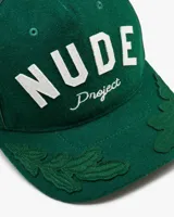 Gorra verde botella de estilo varsity, estructurada, con la inscripción frontal "NUDE Project" bordada en blanco. Presenta detalles de hojas bordadas en tono sobre tono sobre la visera.