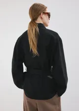 Chaqueta de lino color negro con diseño recto, cuello camisero, manga larga, cierre frontal de botones y cinturón ajustable del mismo material. Incluye forro interior.
