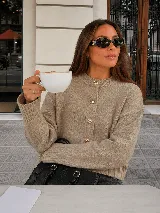 Cardigan de punto color beige con cuello redondo, mangas largas con puños acanalados y cierre frontal con grandes botones dorados texturados.