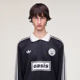 Camiseta Adidas de manga larga en colaboración con la banda Oasis, de color negro con cuello polo, puños y detalles en blanco marfil. Presenta las tres tiras características en las mangas, el logo trébol de Adidas, un escudo circular conmemorativo de la gira 'Live '25' y el estampado con la inscripción 'oasis' en el centro del pecho.
