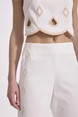 Top crop blanco con bordado y calados en forma de rombos y gotas, con escote redondo y terminación festoneada en el bajo.