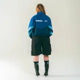 Campera deportiva azul confeccionada en nylon liviano, con paneles diagonales en contraste y micrográfico Kaboa aplicados al frente y un gráfico en la espalda.