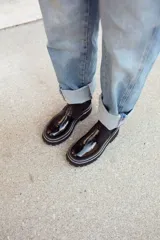 Botas tipo chelsea de cuero negro con textura granulada, paneles laterales elásticos y suela track robusta de goma.