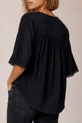 Camisa blanca de lino, con escote en V, mangas tres cuartos con detalles de encaje en los puños, cierre frontal de botones y diseño más largo en la parte trasera.