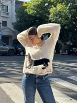 Sweater tejido color crema con cuello y puños acanalados en color naranja. Presenta un diseño bordado de un perro salchicha negro con un moño naranja.