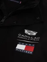 Chaleco negro con cuello chimenea, cierre de cremallera oculto con botones a presión y dos bolsillos laterales ribeteados. Presenta logos bordados en el pecho de Tommy Hilfiger y Cadillac Formula 1 Team.