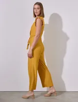 Mono de seda fría color mostaza, con escote en V cruzado, cintura elastizada con lazo de ajuste, espalda con abertura ojal y botón, y forro en el torso a tono.