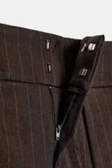 Pantalón de tiro alto con diseño tipo balloon, confeccionado en tela con estampado de rayas verticales. Presenta cintura ancha, pliegues frontales, bolsillos laterales y cierre frontal con cremallera, botón y ganchos metálicos.