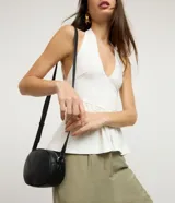 Cartera tipo camera bag marca Satinato de color negro, con forma ovalada, superficie texturizada, cierre superior con cremallera y correa ajustable.