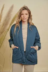 Campera tipo kimono acolchada en color azul petróleo, con diseño de costuras verticales y bolsillos frontales amplios. Presenta mangas largas con puños vueltos y un corte holgado y abierto.