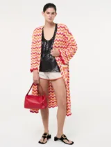 Saco tejido largo con diseño de ondas en tonos naranja, rosa, amarillo y blanco. Tiene bolsillos delanteros y mangas largas acampanadas.