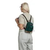 Mochila Jansport modelo Right Pack Mini, color verde oscuro con base de cuero color camel. Presenta un compartimento principal y un bolsillo frontal con cierre, ambos con tiradores de cordón de cuero. Incluye asa superior para colgar.