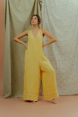 Mono largo de lino color amarillo, con escote en V, tirantes finos y detalles de costuras decorativas blancas en el escote y en los bajos de las piernas anchas.