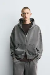 Sudadera con capucha y cierre de cremallera, de corte relajado (relaxed fit), confeccionada en algodón con interior afelpado. Presenta bolsillos frontales tipo canguro y acabados en rib. El tejido tiene un efecto lavado que le da un color negro desgastado.