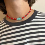 Collar corto de cuentas rojas y turquesas alternadas, con dije central de pez color turquesa.