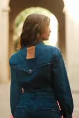 Mono de denim azul con cierre frontal de botones metálicos, cuello camisero, mangas largas y bolsillos delanteros.