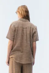 Camisa amplia y relajada de algodón liviano color blanco, de trama abierta y textura, con cuello camisero, mangas cortas y cierre de botones al frente.