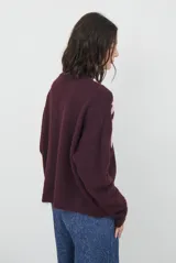 Buzo de tejido de punto en color beige, con cuello redondo y mangas largas. Presenta un delicado bordado de ramas y hojas en color crema en la parte superior del frente.