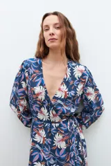 Maxi vestido azul marino con estampado floral en tonos blanco, rosa y azul. Diseño cruzado con lazo en la cintura y mangas largas.