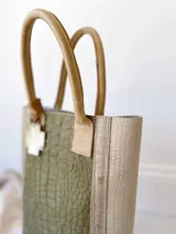 Bolso matero verde con textura croco y detalles en beige. Tiene doble asa corta y accesorio metálico en forma de cruz.