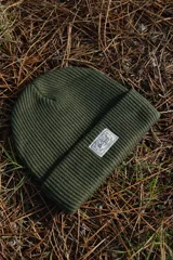 Gorro de lana verde oliva tejido en acrílico con etiqueta bordada con el logo de la marca.