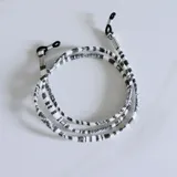 Cuerdita para lentes de tela tejida con patrón de rayas blancas y negras, con terminales metálicos y sujetadores de goma ajustables.
