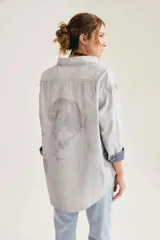Camisa oversize de algodón con textura de cuadrillé sutil, cuello clásico, bolsillo frontal y mangas largas con puños vueltos que revelan un forro interior a cuadros.