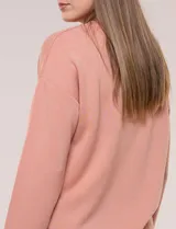 Buzo color salmón de punto suave, con cuello redondo y detalles calados de crochet. Cuenta con mangas largas y diseño holgado.