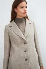 Saco corto entallado de lana fina, con cuello solapa, manga larga y cierre frontal con botones. Presenta un diseño clásico con textura de espiga en tonos tierra.