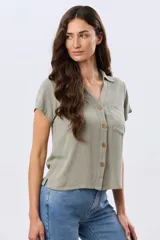 Camisa lisa de lino color beige, de manga corta, con cuello camisero, bolsillo ojal en el pecho y cierre frontal con botones.