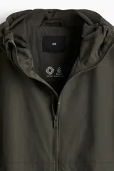 Campera rompevientos de nylon color verde oscuro, con capucha ajustable con cordón, cierre frontal y puños elásticos. Presenta bolsillos laterales y un bolsillo interior, todos con cierre.