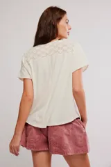 Remera henley de algodón liviano y jaspeado, de calce relajado, color blanco off-white, con mangas cortas, botonadura al cuello, aplicaciones de encaje y ruedo enrollado.