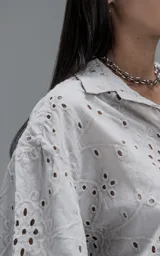 Camisa de manga corta y corte holgado con diseño de bordado broderie en toda la prenda, cuello camisero y cierre frontal de botones.