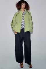Cazadora ZARA Woman Collection color verde militar, con cuello alto, manga larga y bolsillos frontales. Cuenta con detalles de vivos a contraste en los hombros, bajo elástico asimétrico y cierre frontal oculto con cremallera y botones.