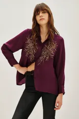Camisa de viscosa color violeta con cuello clásico, manga larga y cierre frontal con botones. Presenta un diseño bordado con lentejuelas doradas en ambos lados del pecho.