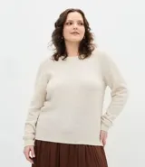 Suéter de punto color beige con cuello redondo, manga larga y aplicaciones de perlas distribuidas por toda la prenda. Presenta puños y ruedo acanalados.