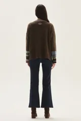 Sweater tejido de lambswool color beige, con cuello redondo y puños acampanados con rayas de colores (marrón, mostaza, bordó y beige). Incluye un detalle de temporada hecho a mano en la espalda.