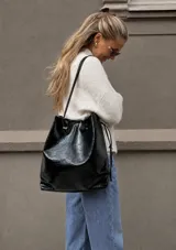 Cartera tipo shopper de cuero sintético con acabado brillante y efecto arrugado, de color negro, con diseño flexible y tirantes delgados para el hombro.